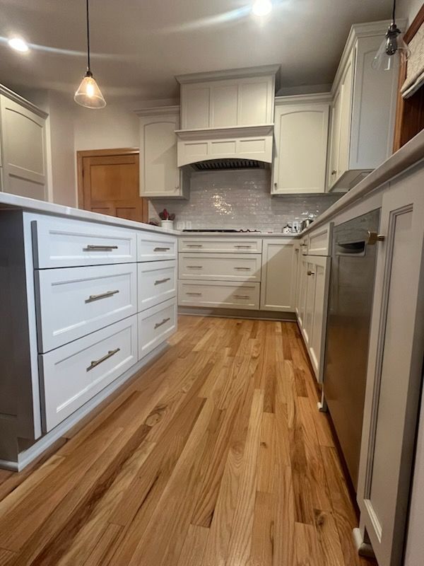A kitchen with white cabinets and hardwood floors.