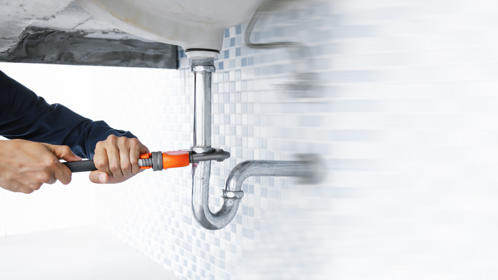 A plumber is fixing a sink pipe with a wrench.