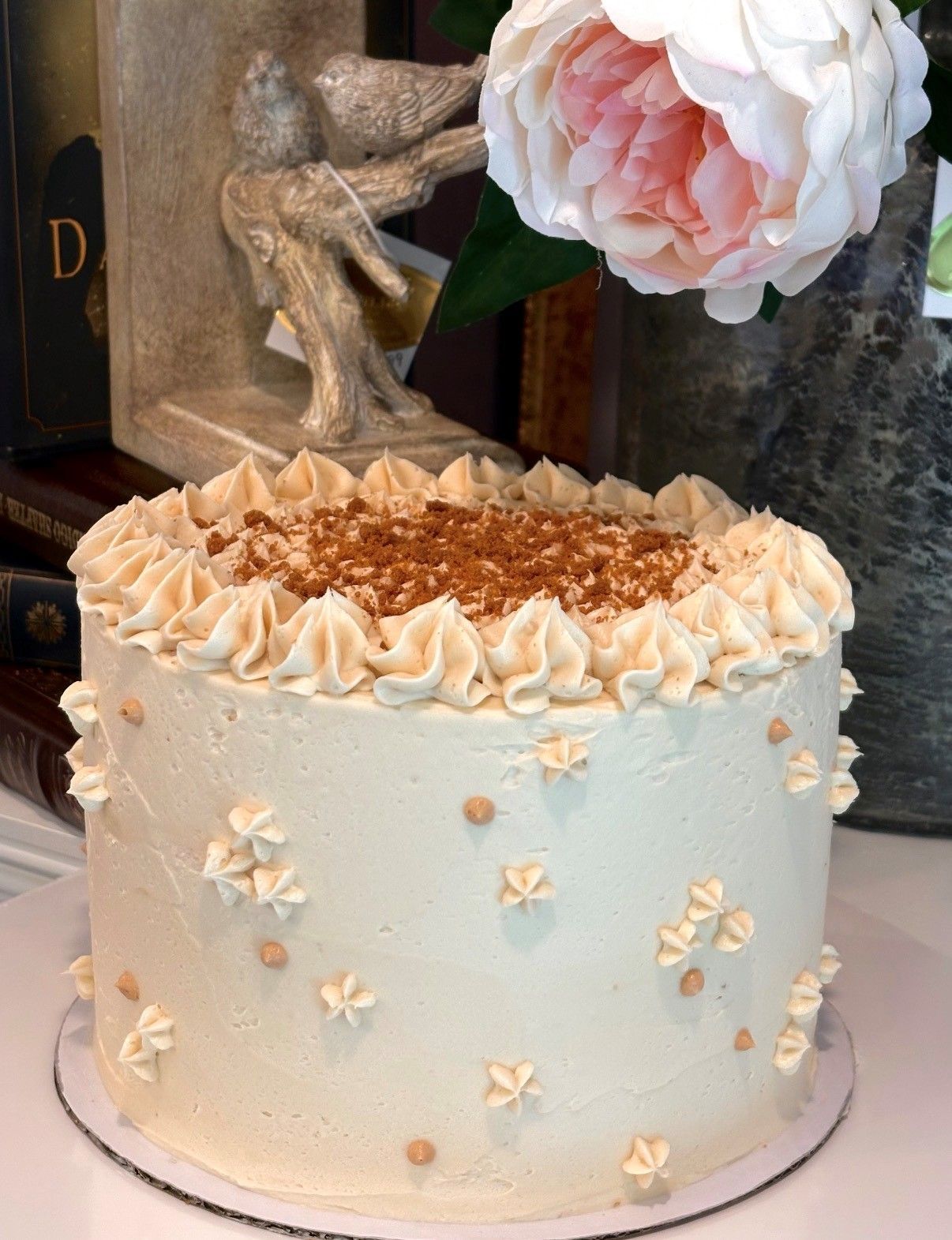 Cream frosted cake with piped rosettes and white flower decorations on a table.