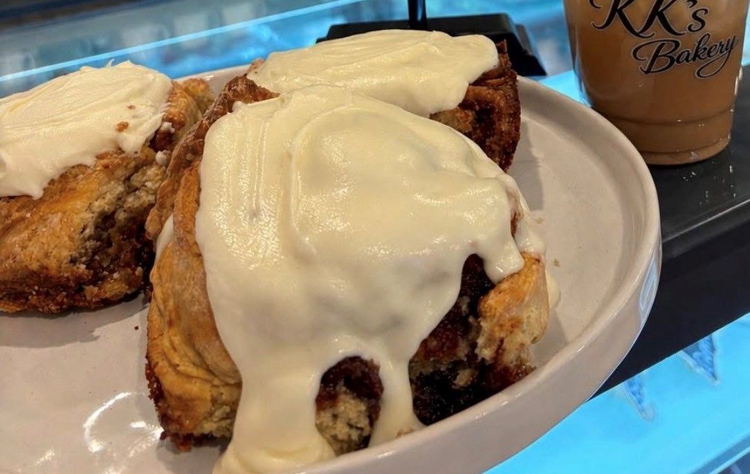 Iced cinnamon rolls on a white plate, with a coffee cup in the background.