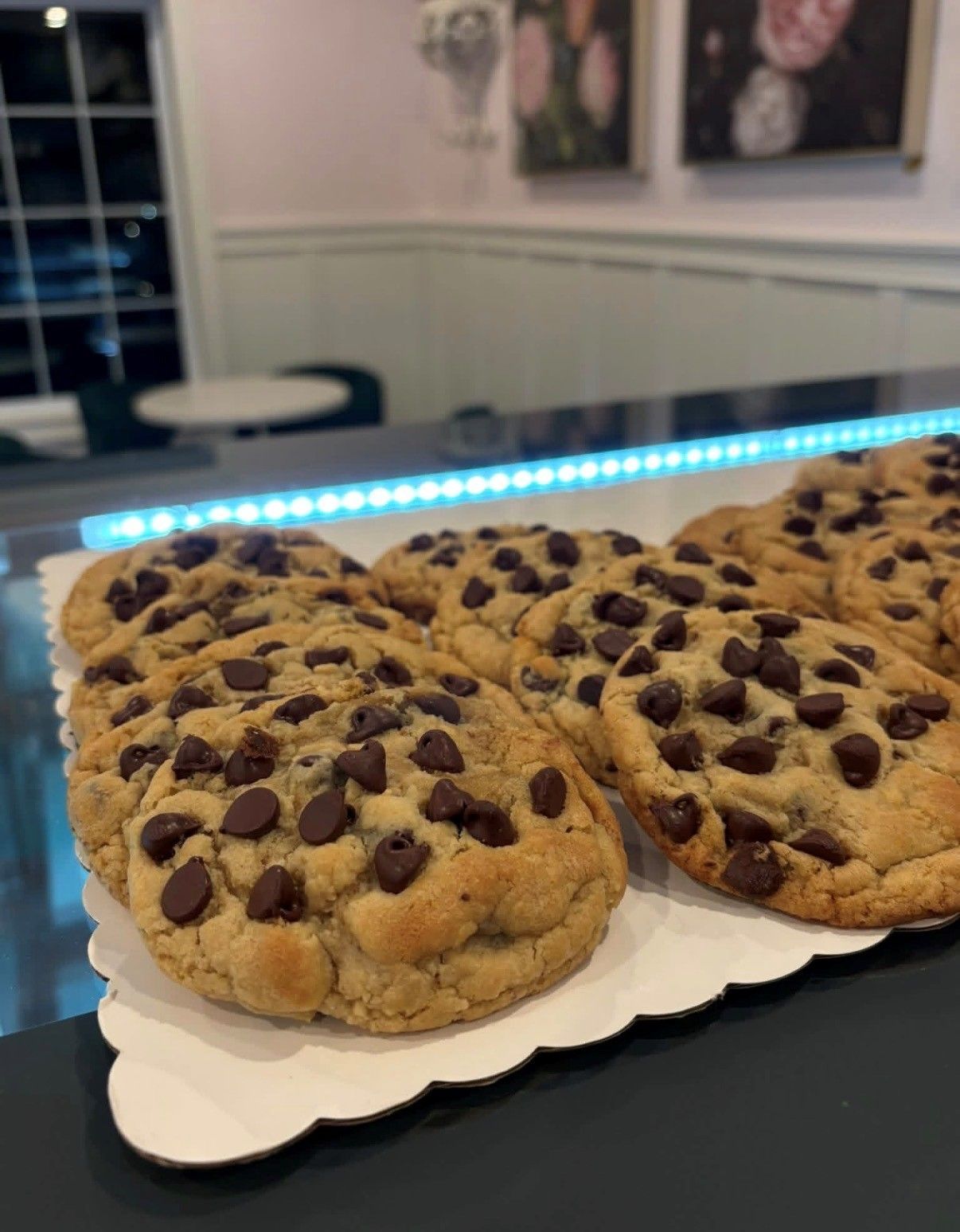 Two large chocolate chip cookies on a white scalloped tray in a kitchen or dining area