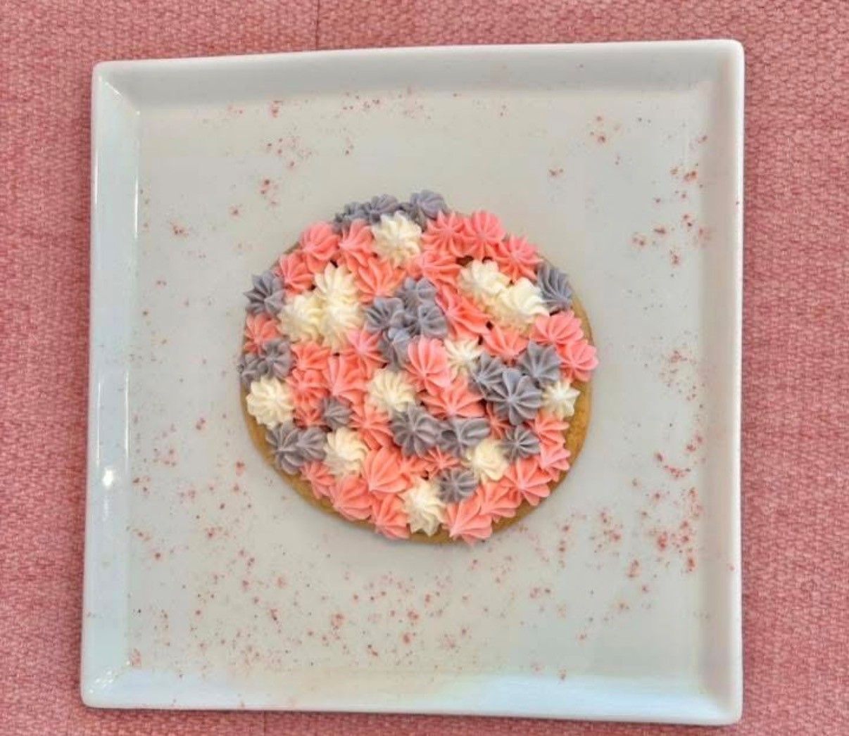 Round floral brooch in pink, peach, cream, and gray on a white square plate over a pink background