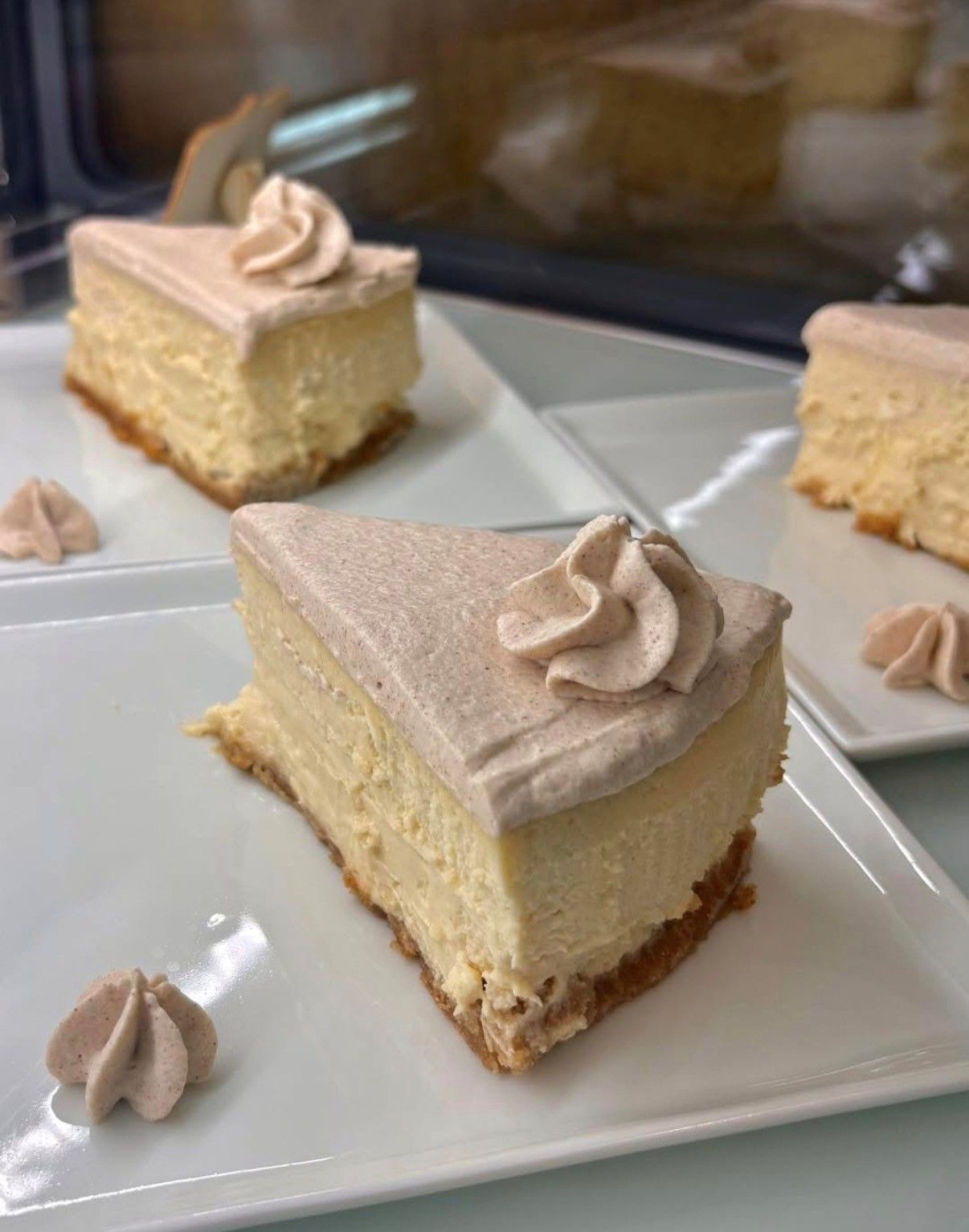 Slices of layered cake with beige frosting on white plates by a window