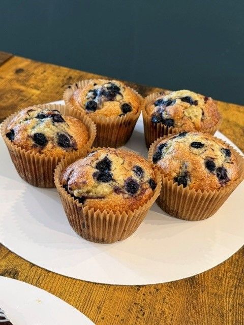 Five blueberry muffins on a white plate on a wooden table