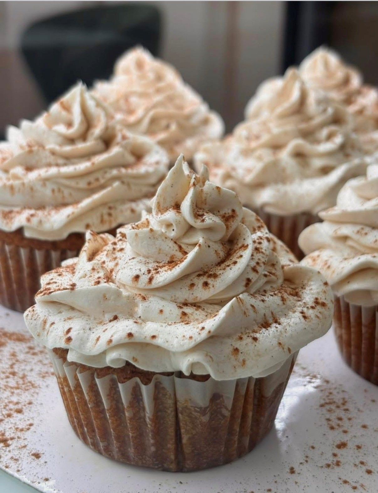 Cupcakes topped with swirled white frosting and cinnamon sprinkles, arranged on a surface