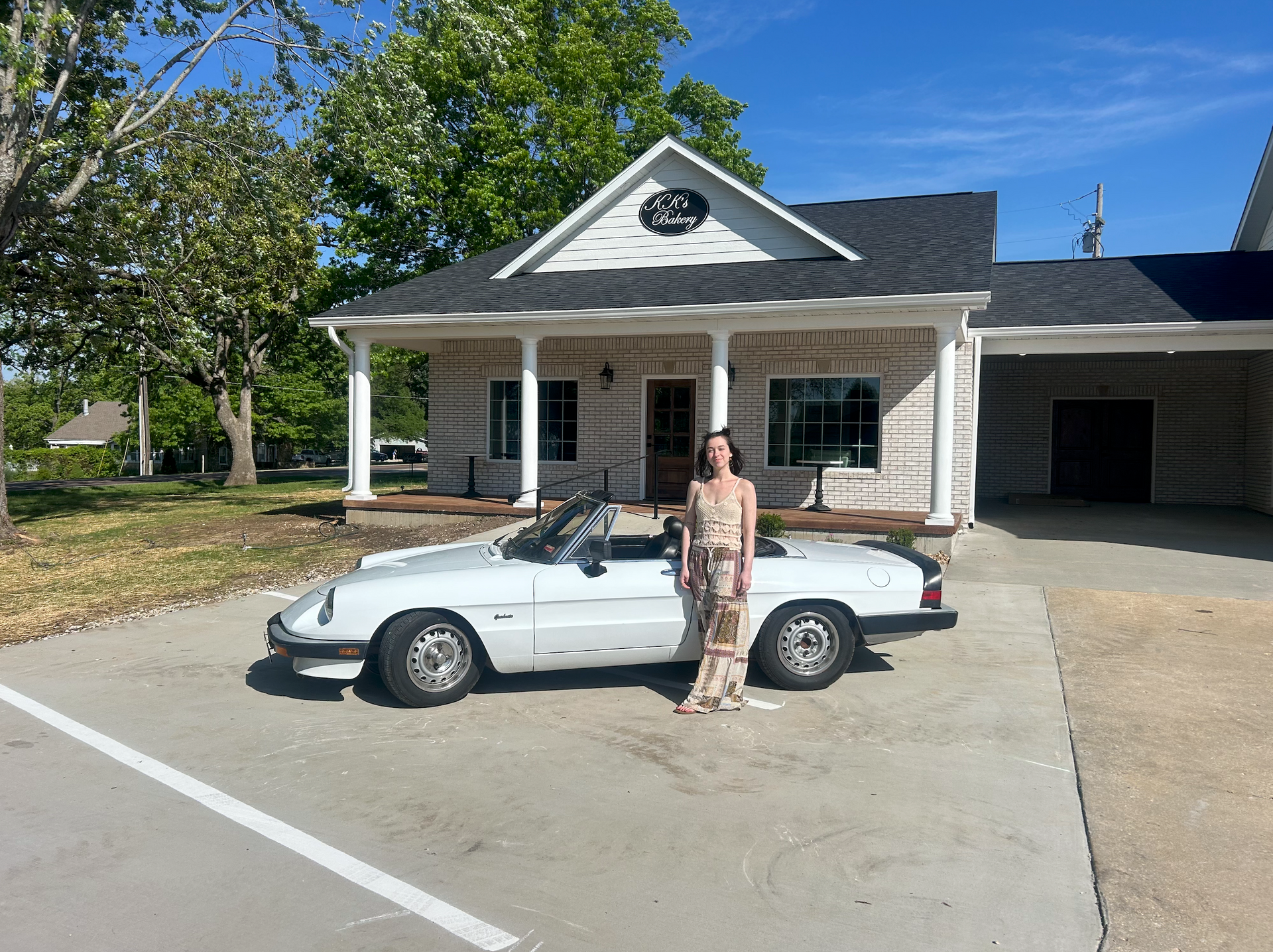Person standing beside a white convertible in front of a house with a porch and garage.