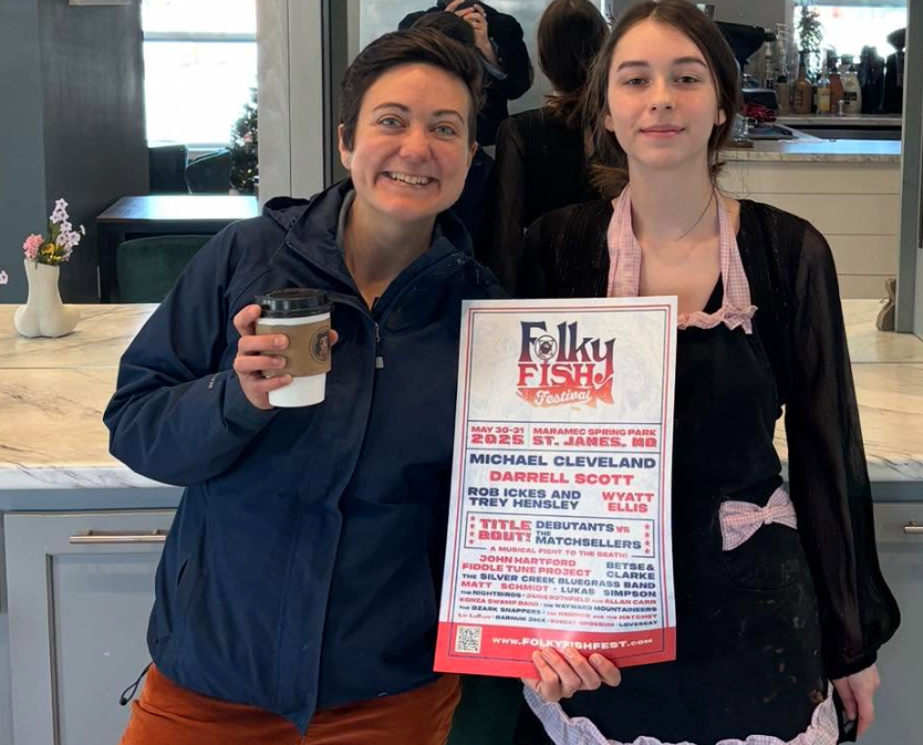 Two people holding a flyer and drink in a bright indoor setting, smiling at the camera.