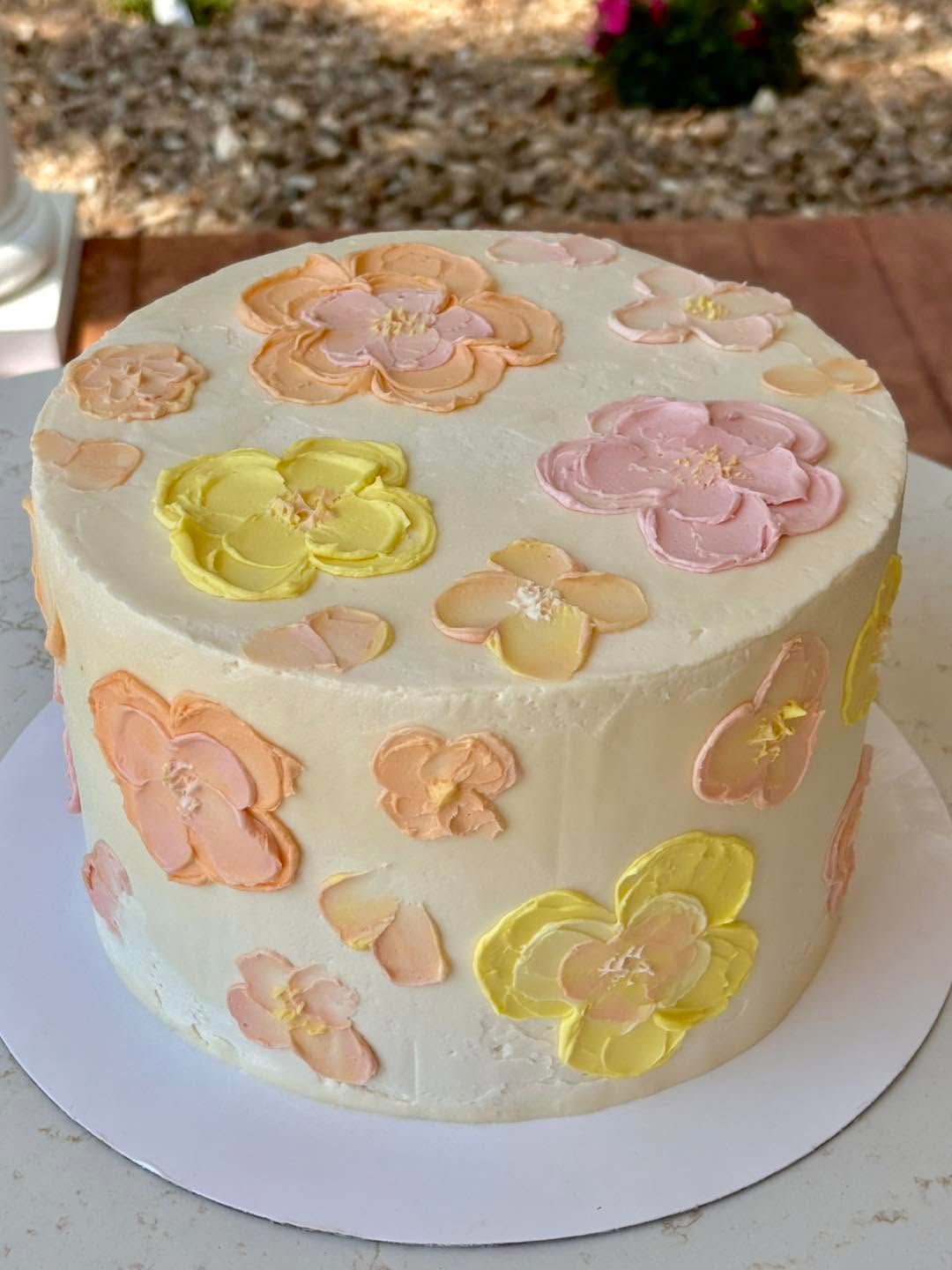 Pastel flower-decorated cake on a white stand outdoors