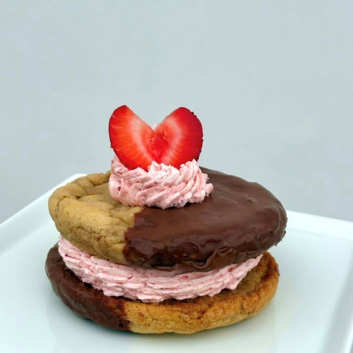 Heart-shaped strawberry dessert on a layered pastry with pink frosting and chocolate glaze