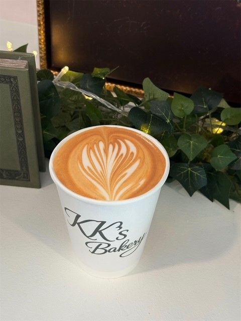 Latte with heart latte art in a white cup on a counter with green ivy behind it
