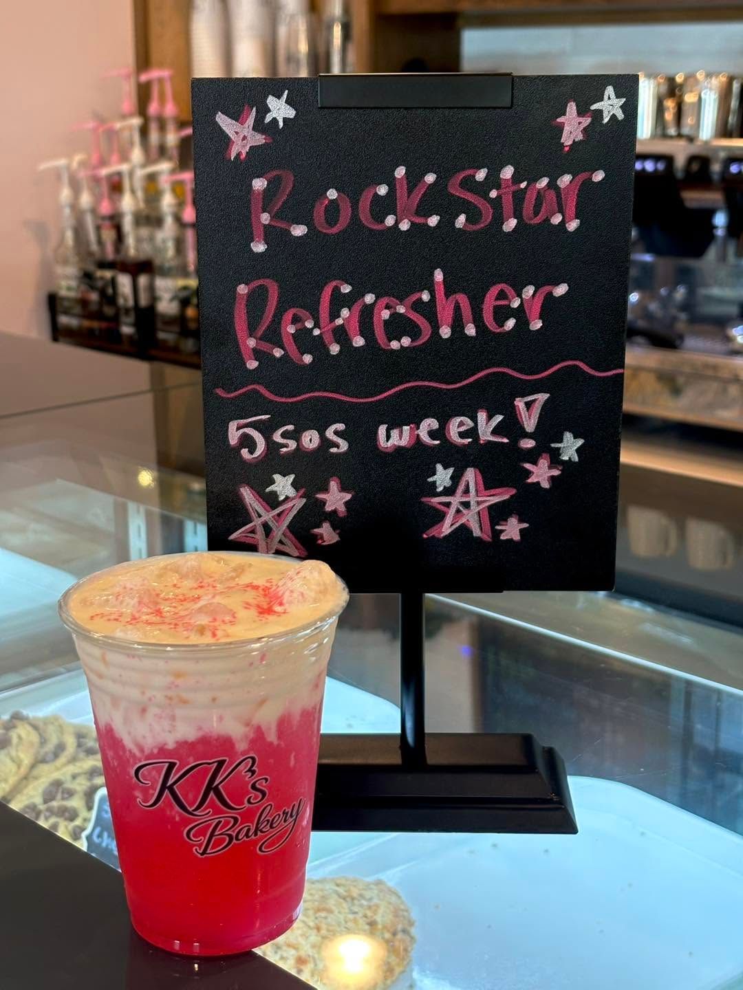 Pink drink in a cup beside a chalkboard sign reading “Rock Star Refresher” and “$5 as week.”