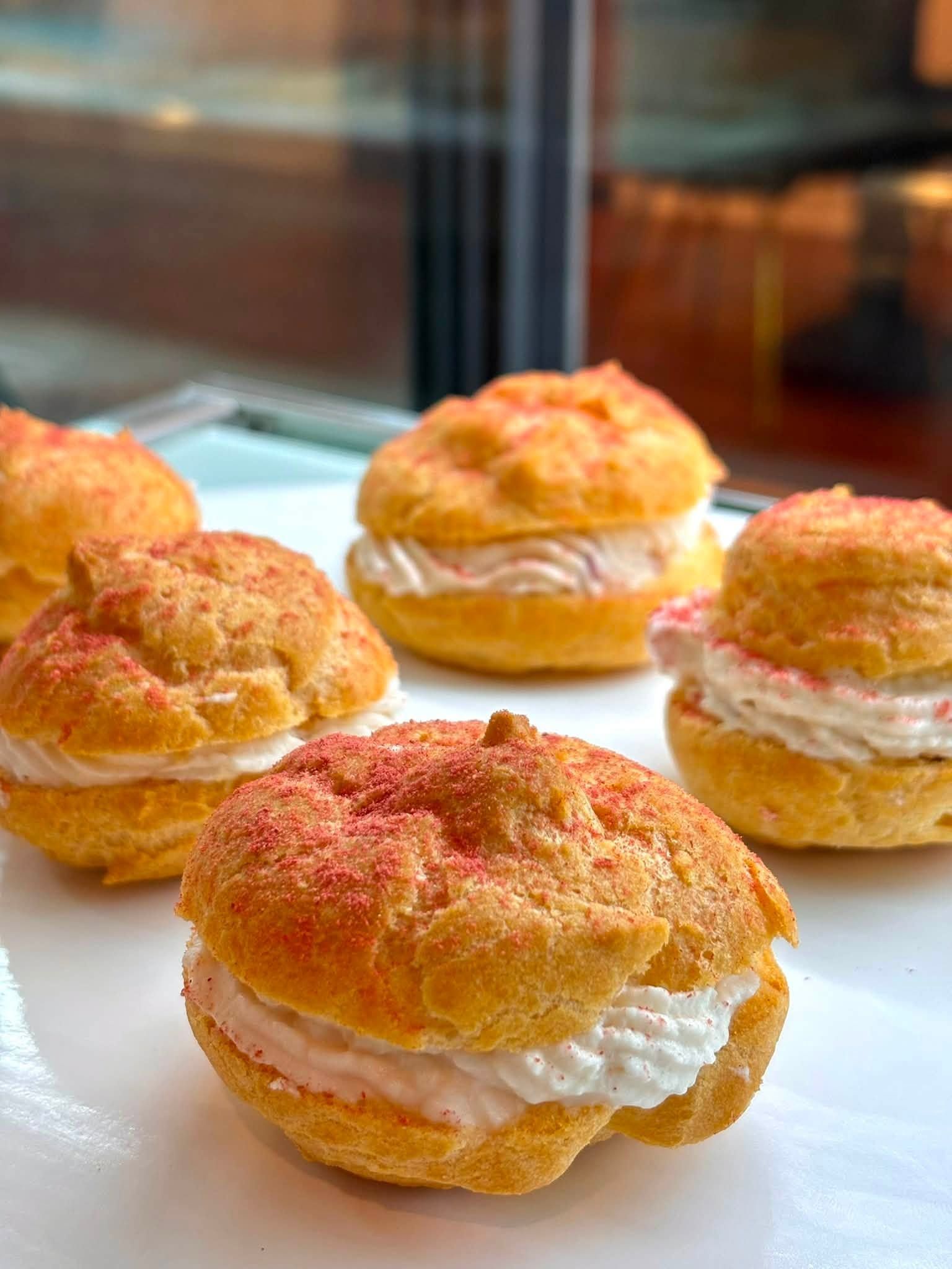 Assorted cream-filled pastries dusted with sugar on a tray by a window