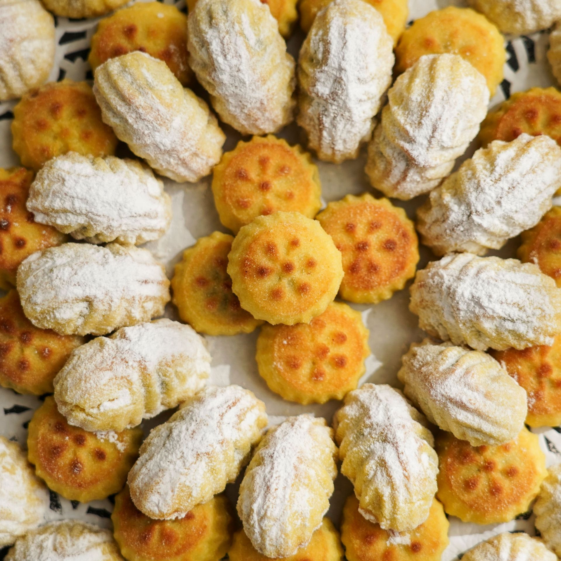 Assorted golden cookies dusted with powdered sugar, arranged in a flower pattern