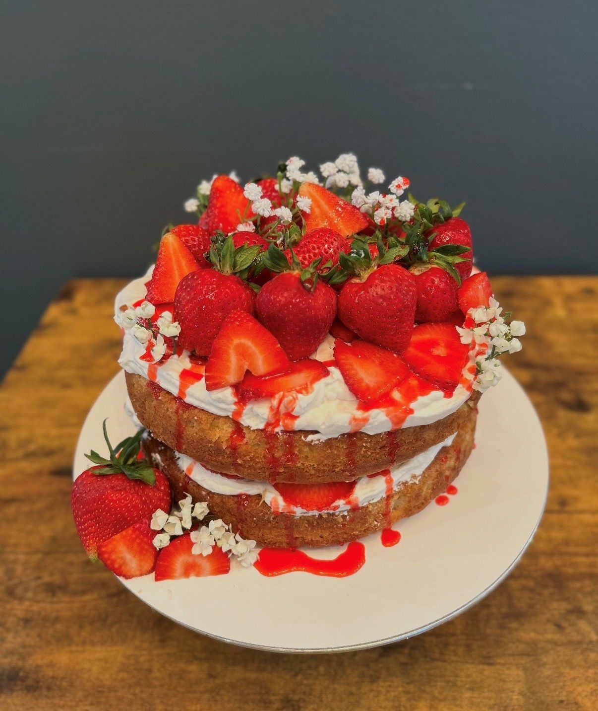 Strawberry layer cake topped with whipped cream and fresh strawberries on a white plate