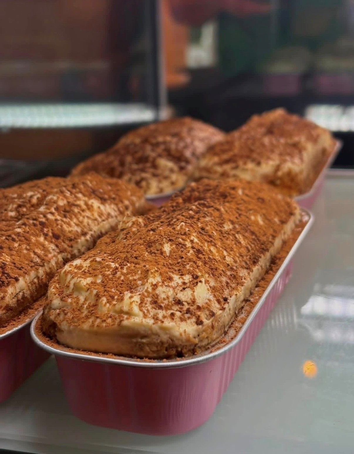Tray of cinnamon-topped loaf cakes on a glass counter in a bakery display
