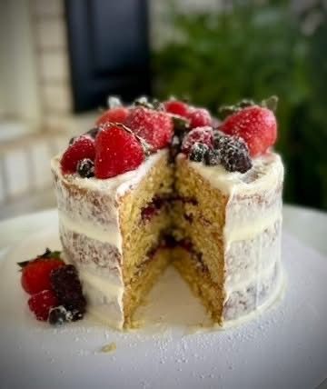Layered berry-topped cake with a slice cut out, showing white frosting and yellow sponge