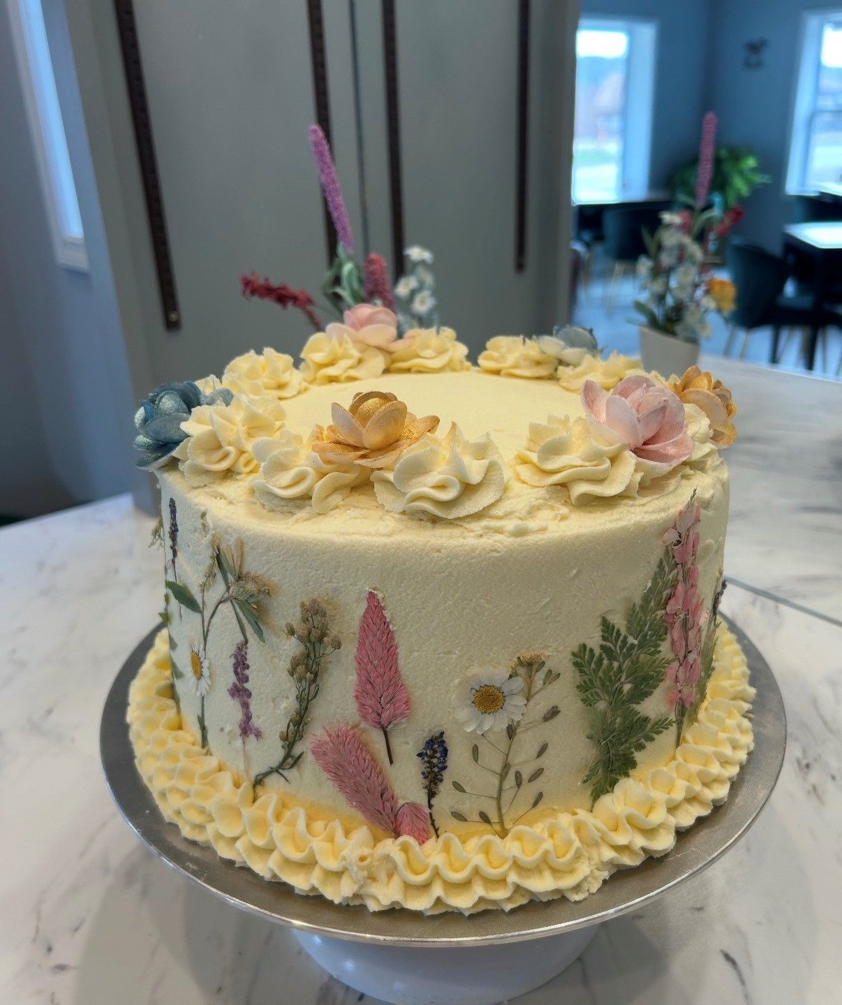 Pastel floral frosted cake on a silver stand in a bright kitchen