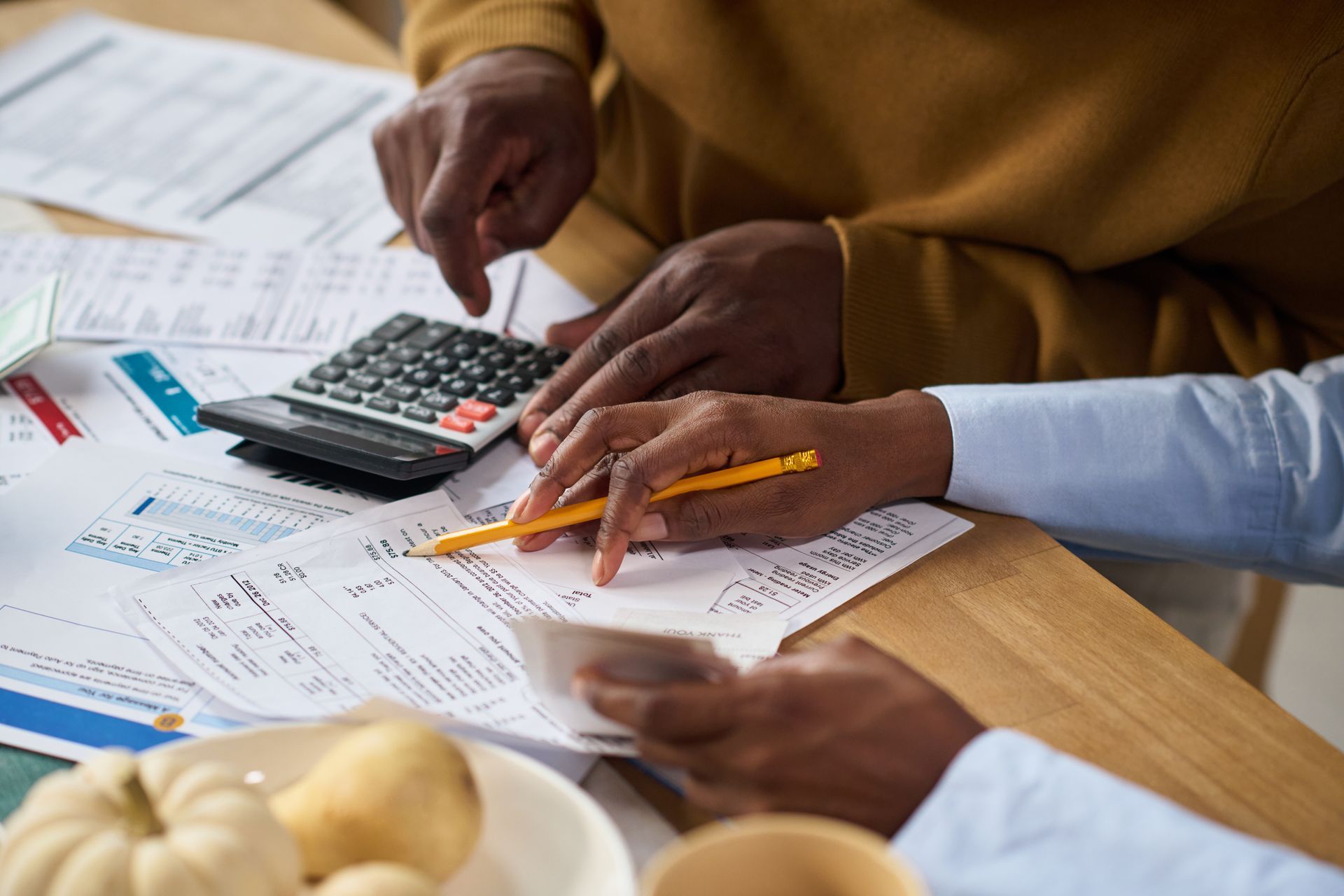Des mains manipulent des factures et utilisent une calculatrice. Une main tient un crayon et pointe du doigt, l'autre utilise la calculatrice.