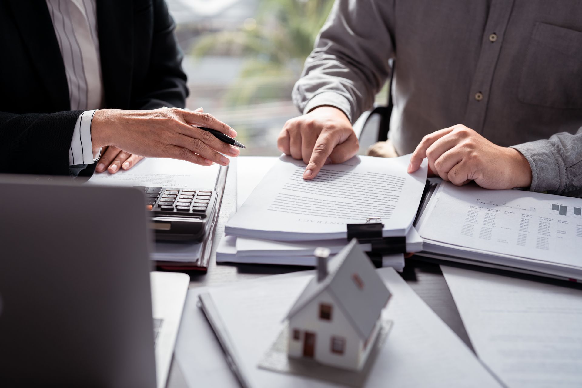 Des personnes examinant des documents à un bureau, une calculatrice et une maquette de maison.