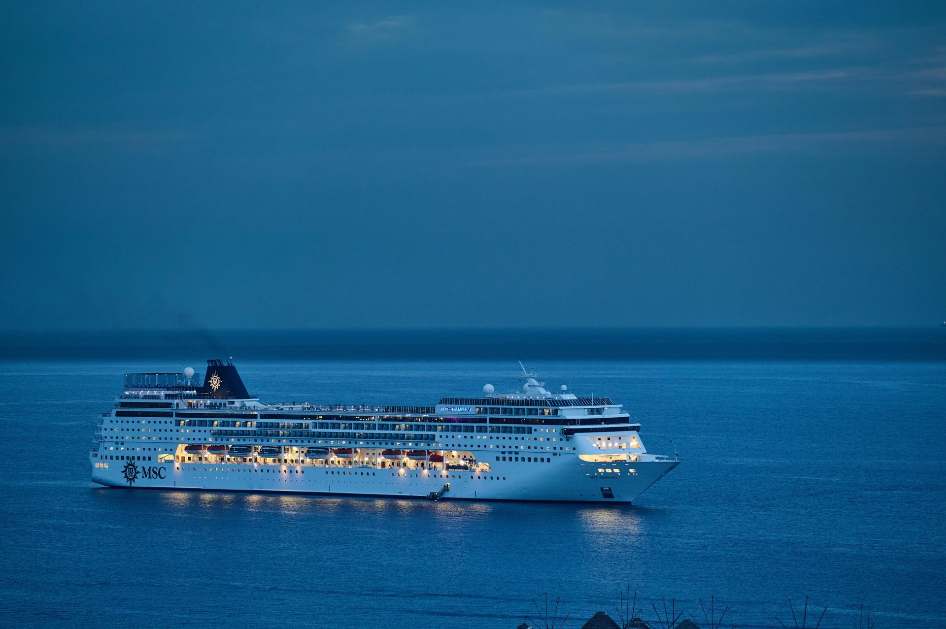 Large white cruise ship lit up on calm blue water at dusk