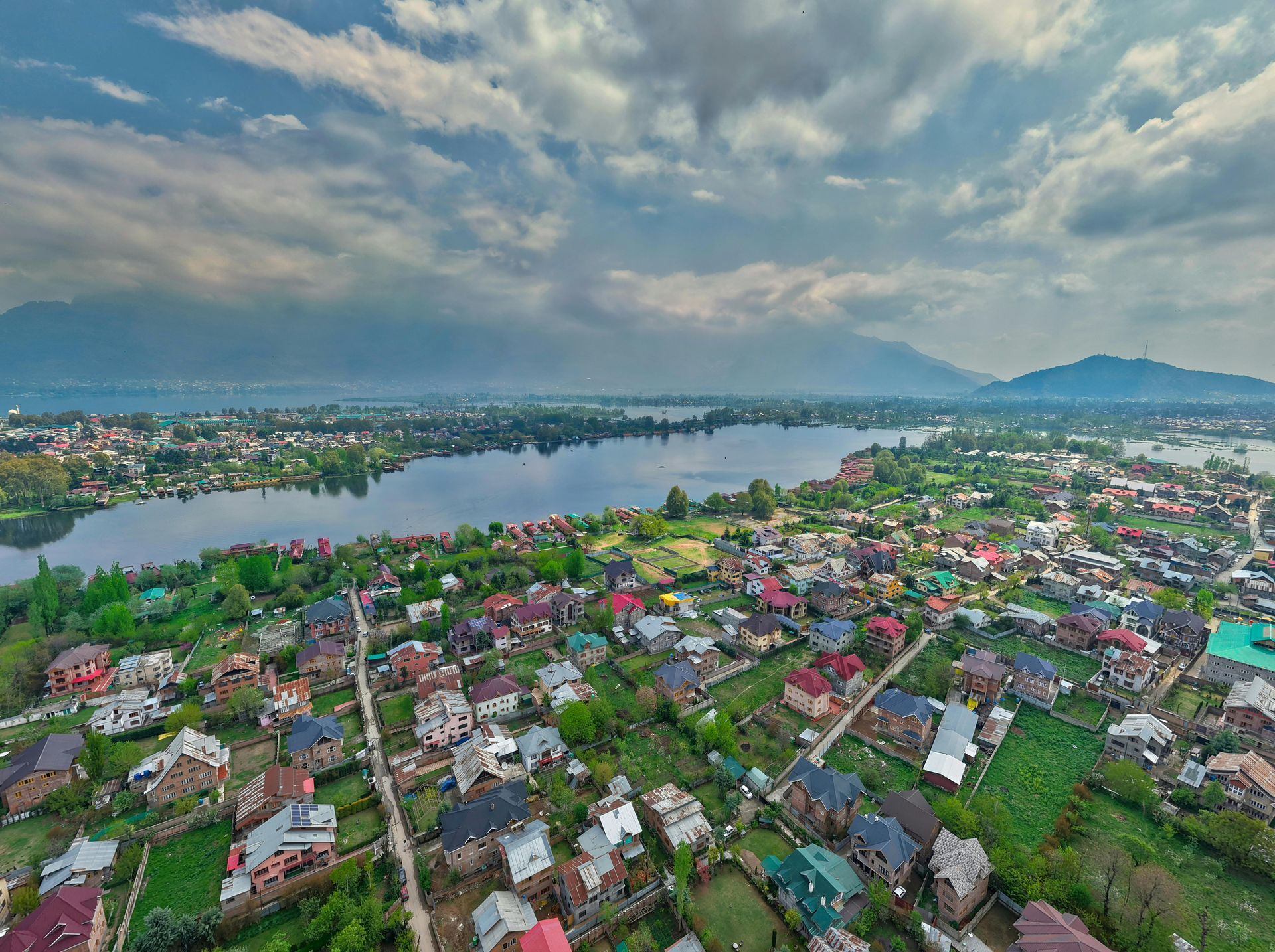 Aerial view of a lakeside town with dense houses, a winding river, and cloudy sky