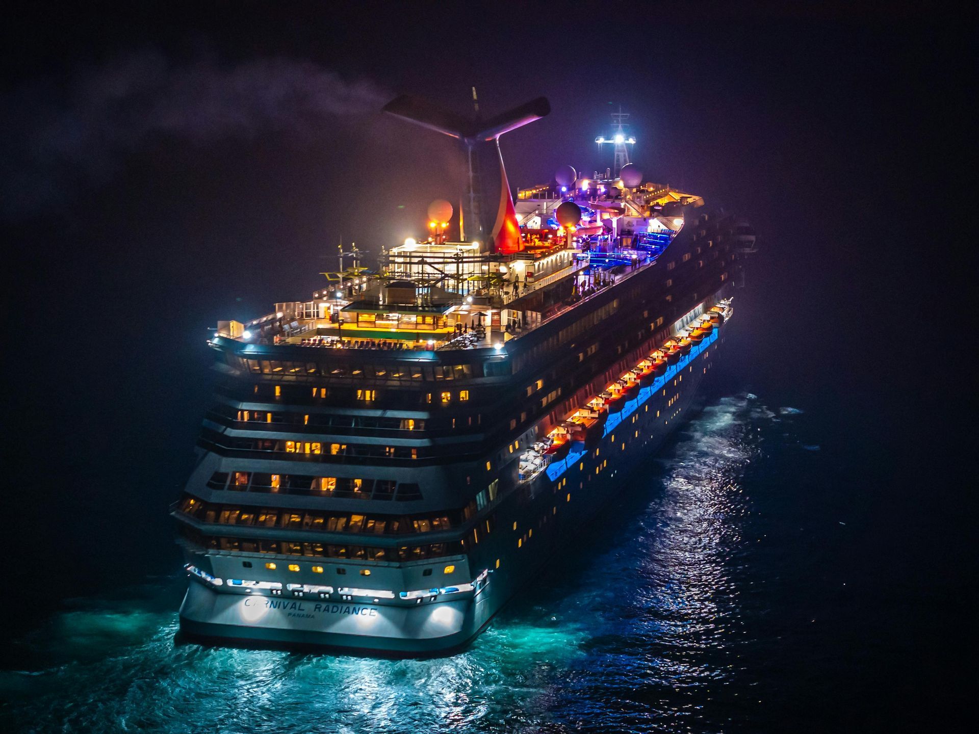 Illuminated cruise ship sailing at night on dark water with colorful deck lights