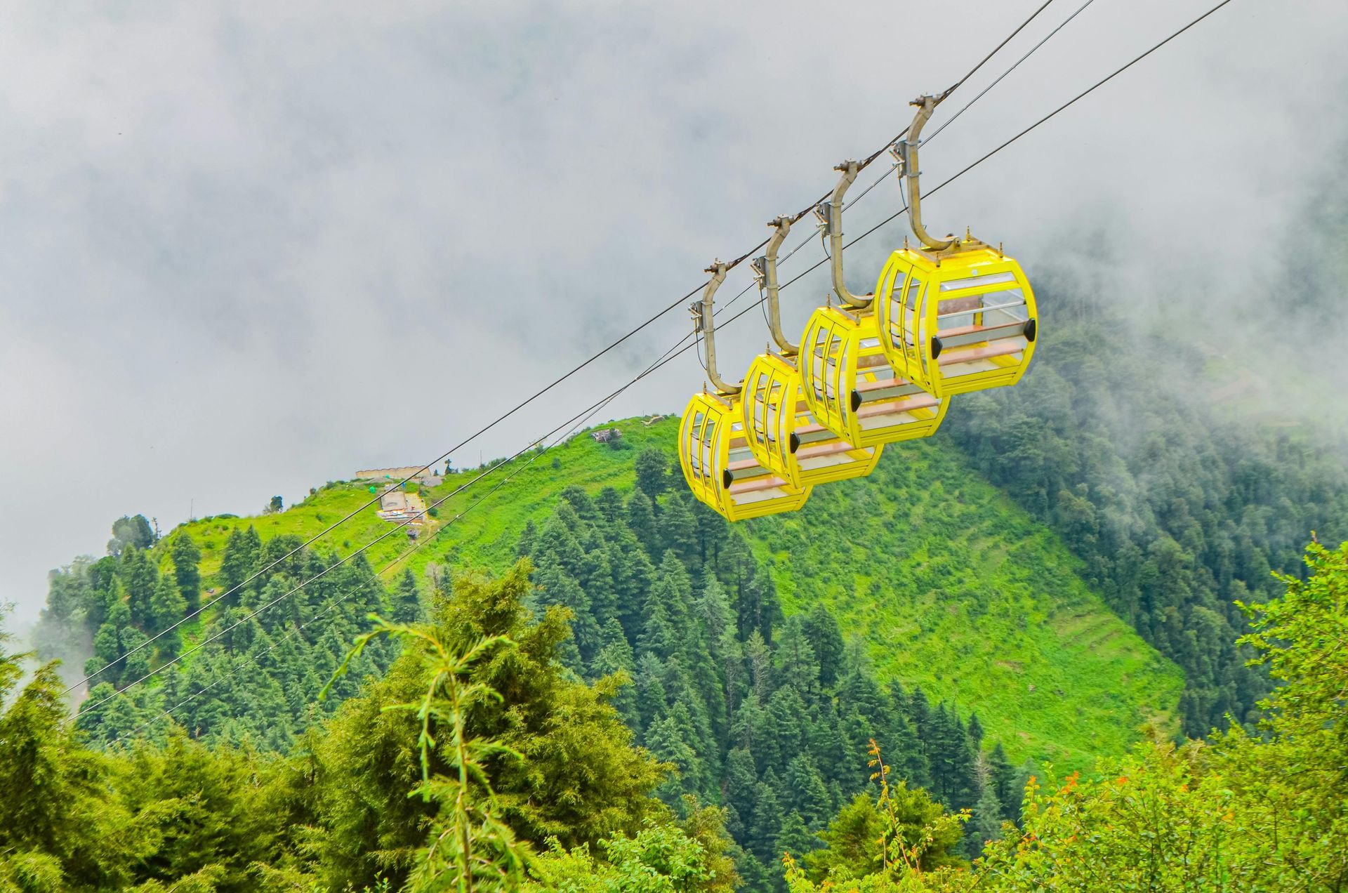 Yellow cable cars on a mountain line above green hills and misty clouds