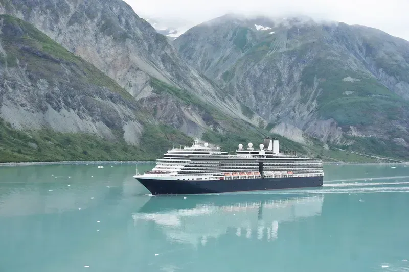 Cruise ship on turquoise water beside steep, misty mountain cliffs