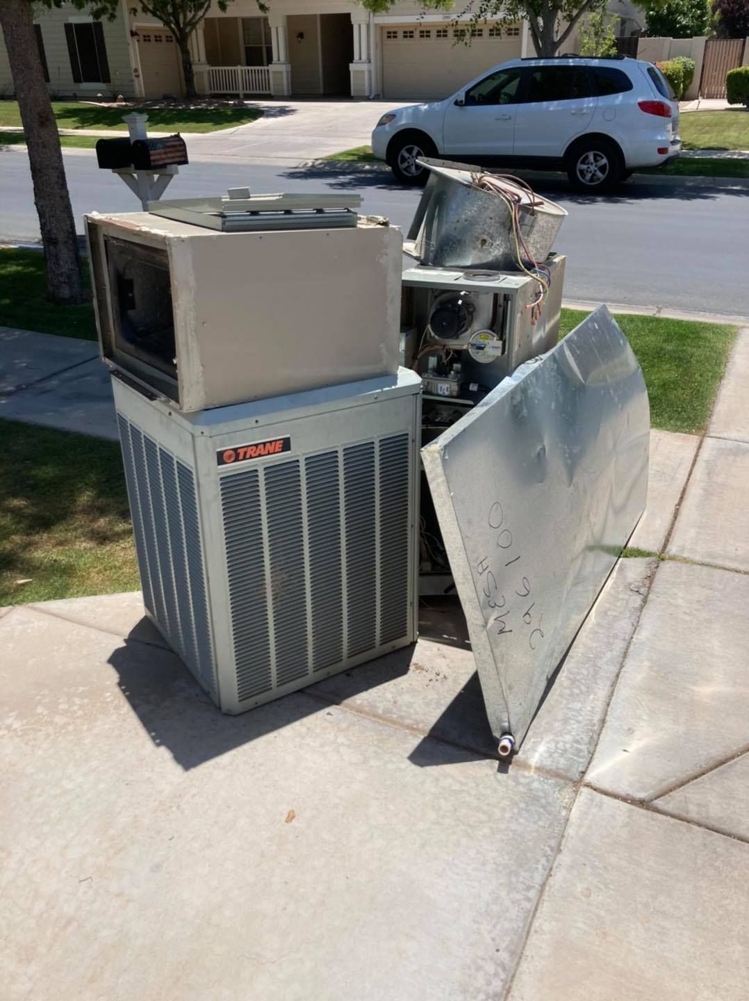 A broken air conditioner is sitting on the sidewalk next to a car.