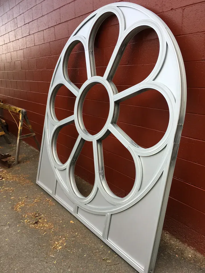 A large white flower shaped window frame is sitting in front of a red brick wall.