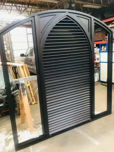A large mirror with shutters on it is sitting in a room next to a car.