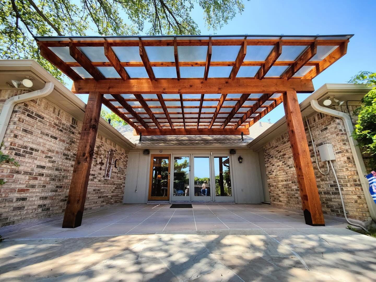 A covered outdoor patio entryway with a wood pergola, brick walls, and glass doors on a sunny day.