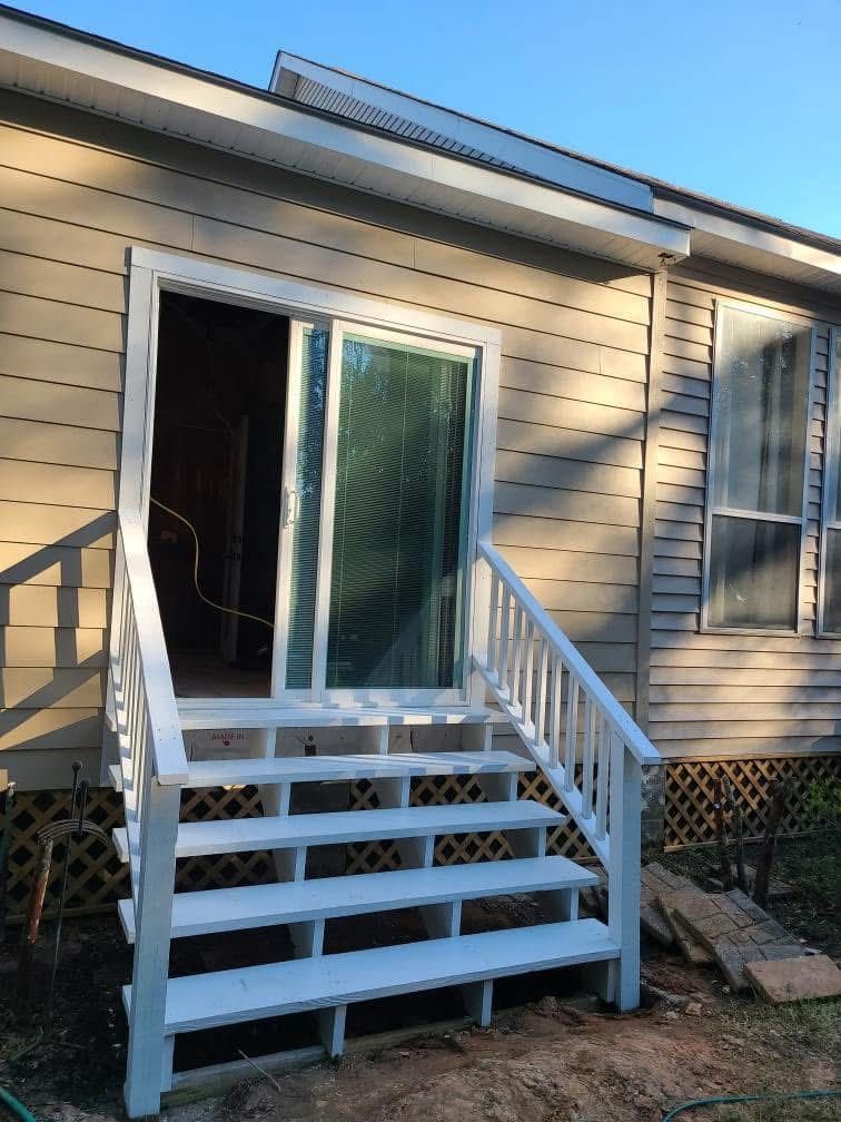 A set of freshly painted white wooden stairs leading to an open sliding glass door on the side of a beige house.