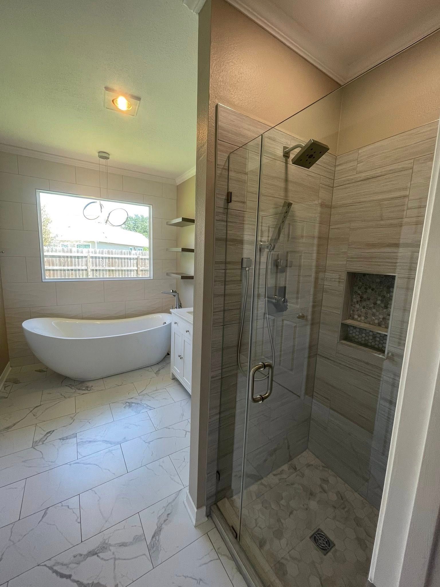 A bathroom featuring a glass-enclosed walk-in shower with a rain head and a freestanding white tub near a large window.