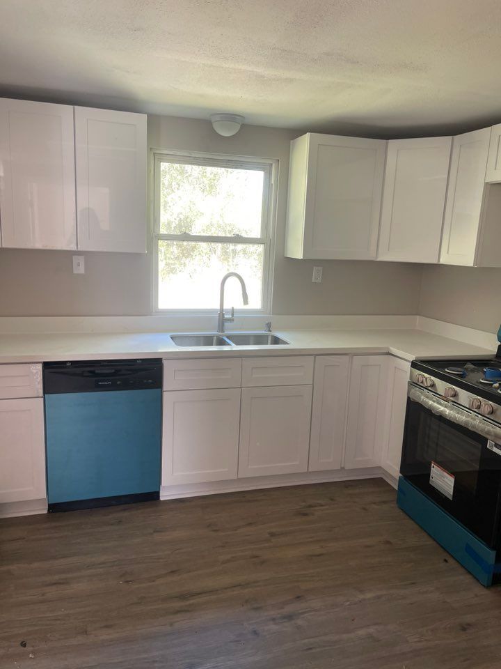 A kitchen featuring white cabinets, white countertops, a blue dishwasher, a stainless steel oven, and light wood flooring.