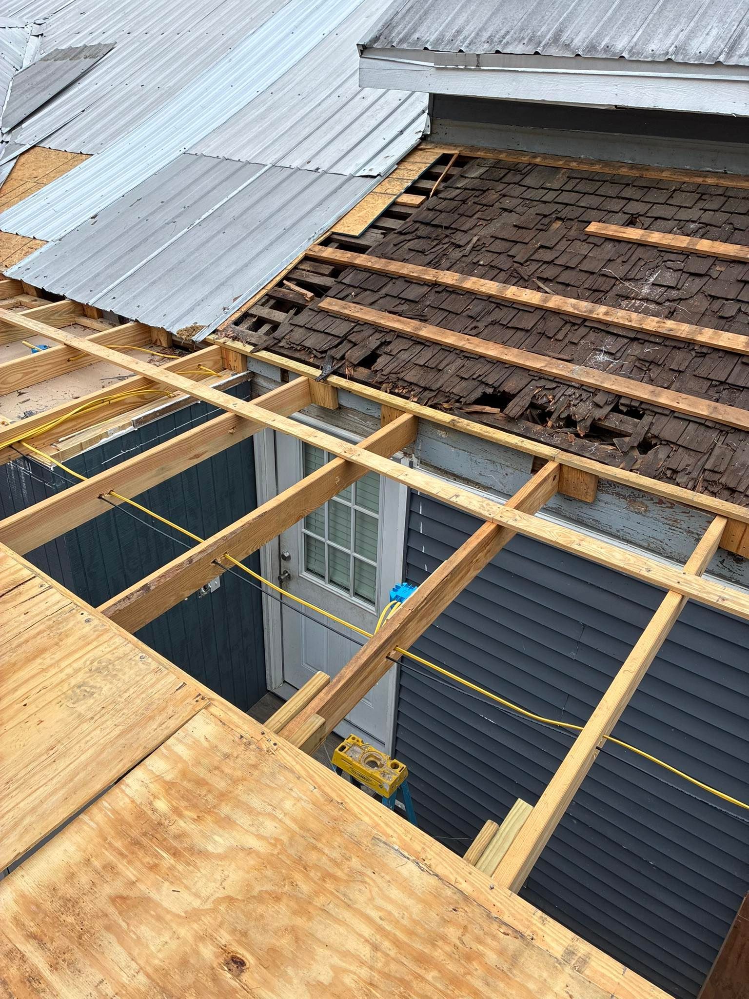 An elevated view of a roof under construction, showing wooden support rafters, a section of metal roofing, and dark sheathing.