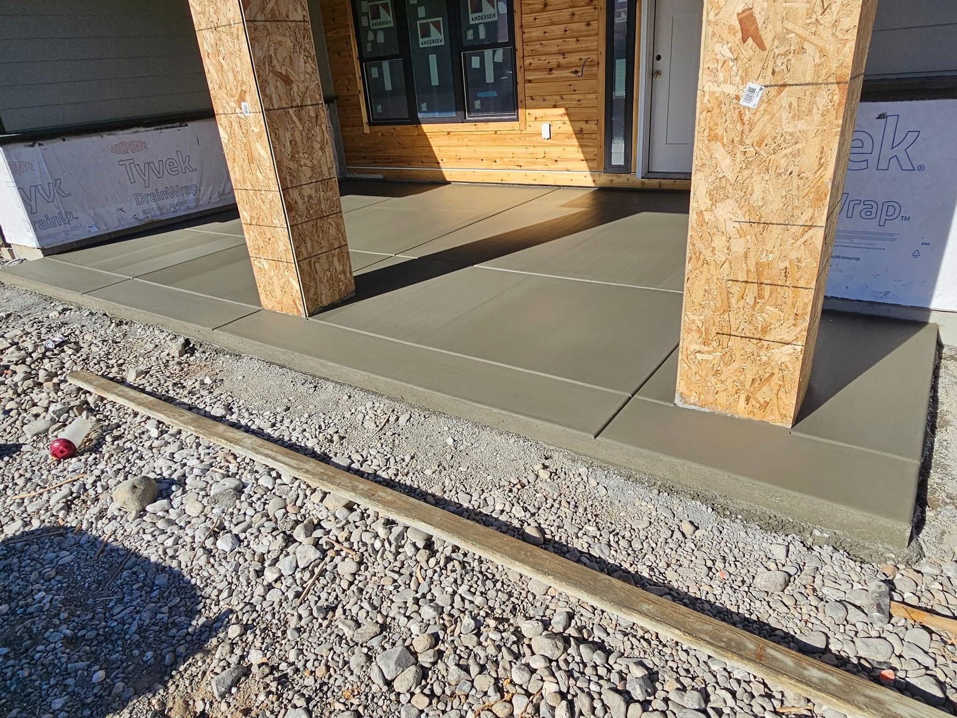 Newly poured concrete porch with two support pillars at the front of a building under construction.