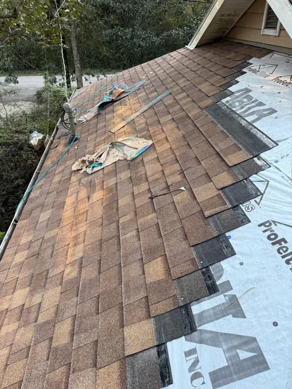 A roof partially covered in new brown shingles next to exposed underlayment with building materials scattered on the slope.
