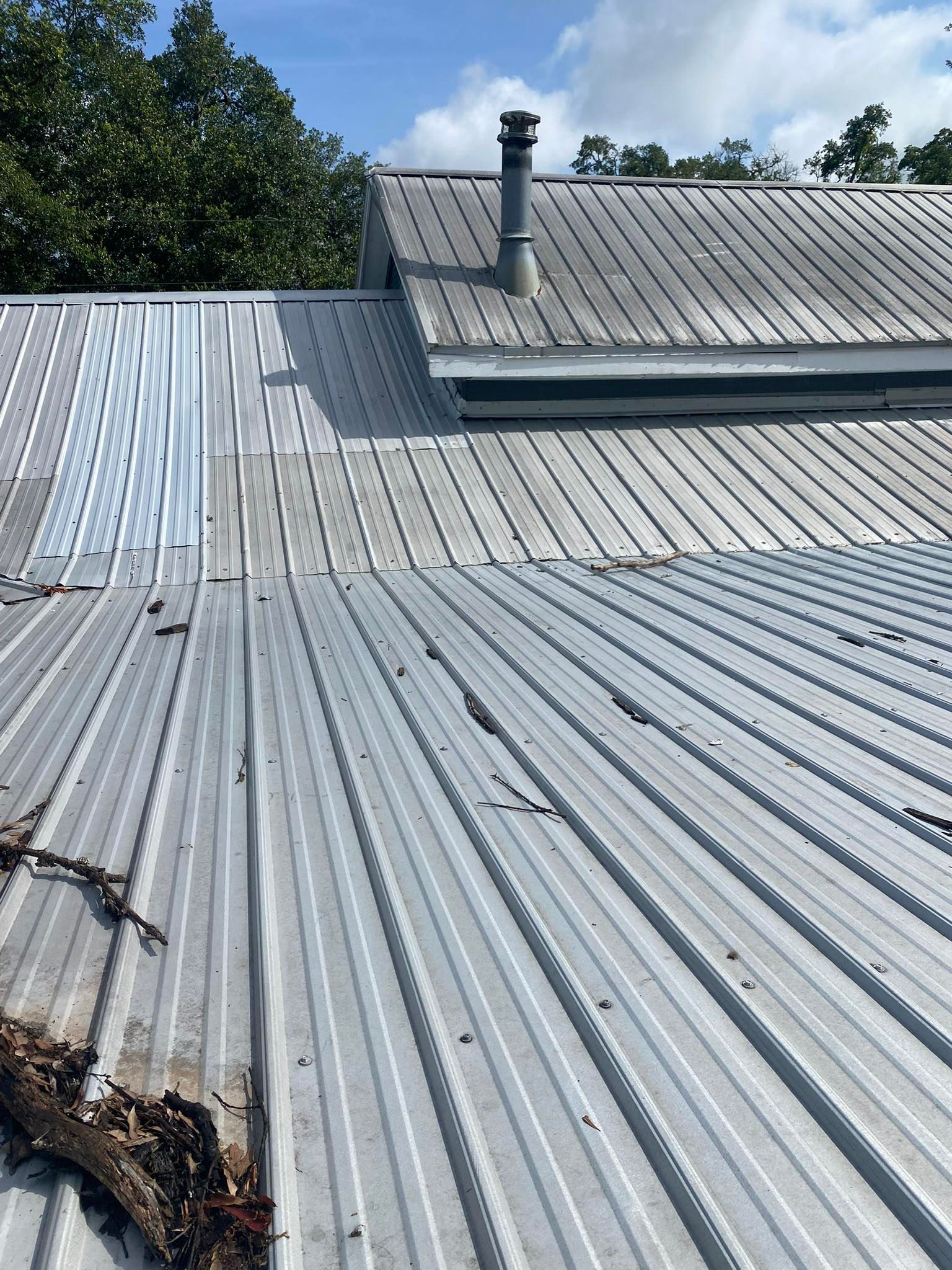 A corrugated metal roof with a chimney, a valley, and some debris scattered along the left side.