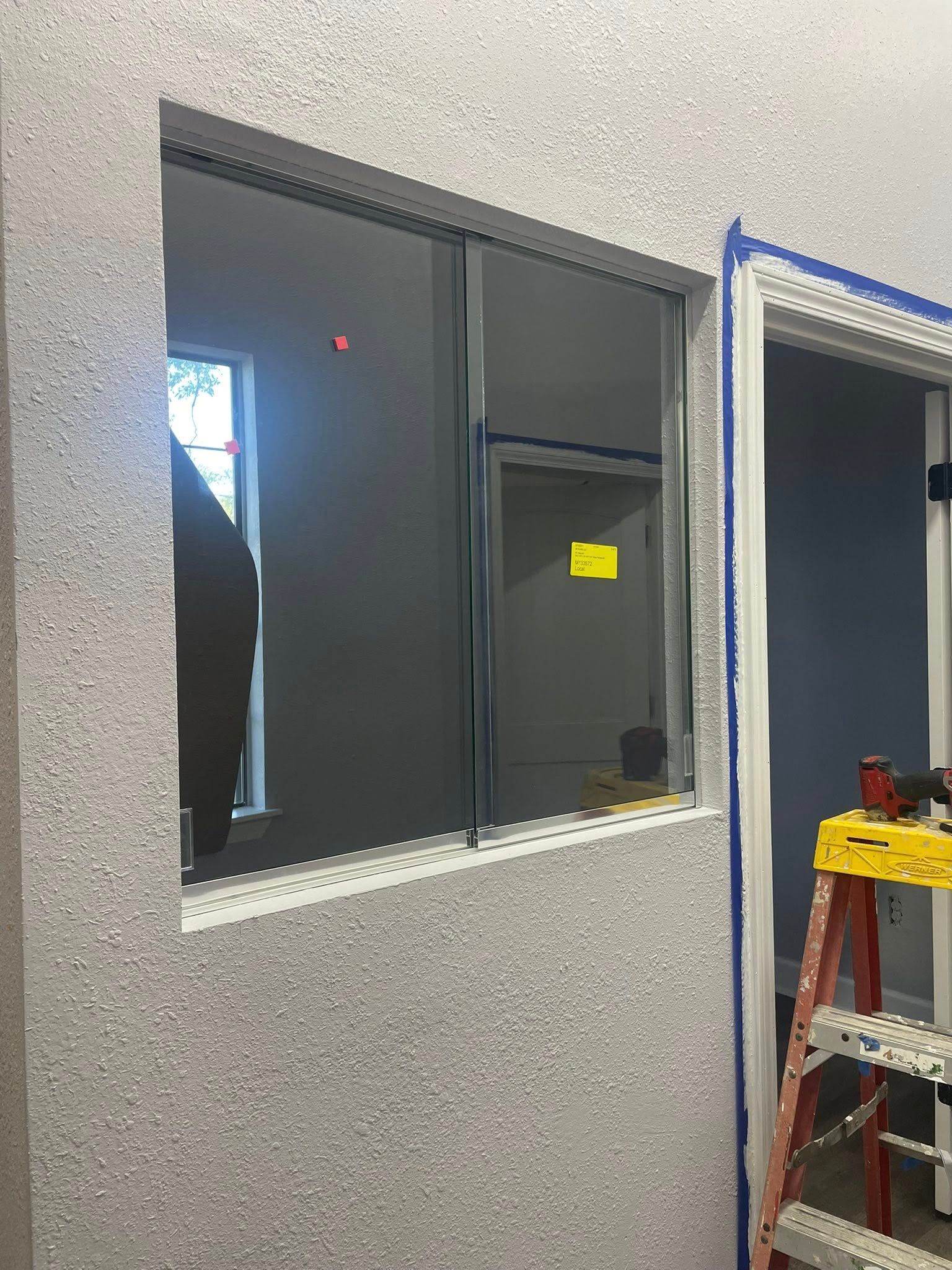 A rectangular dark-tinted window installed in a light gray speckled wall next to a partially visible ladder and doorway.