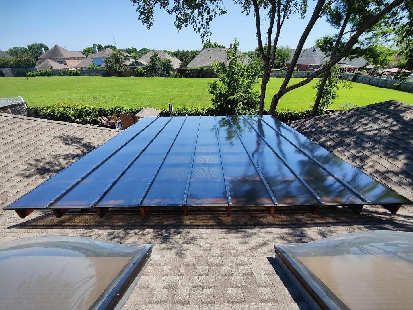 A sleek, dark, rectangular solar panel installation on a textured residential roof overlooking a grassy backyard.