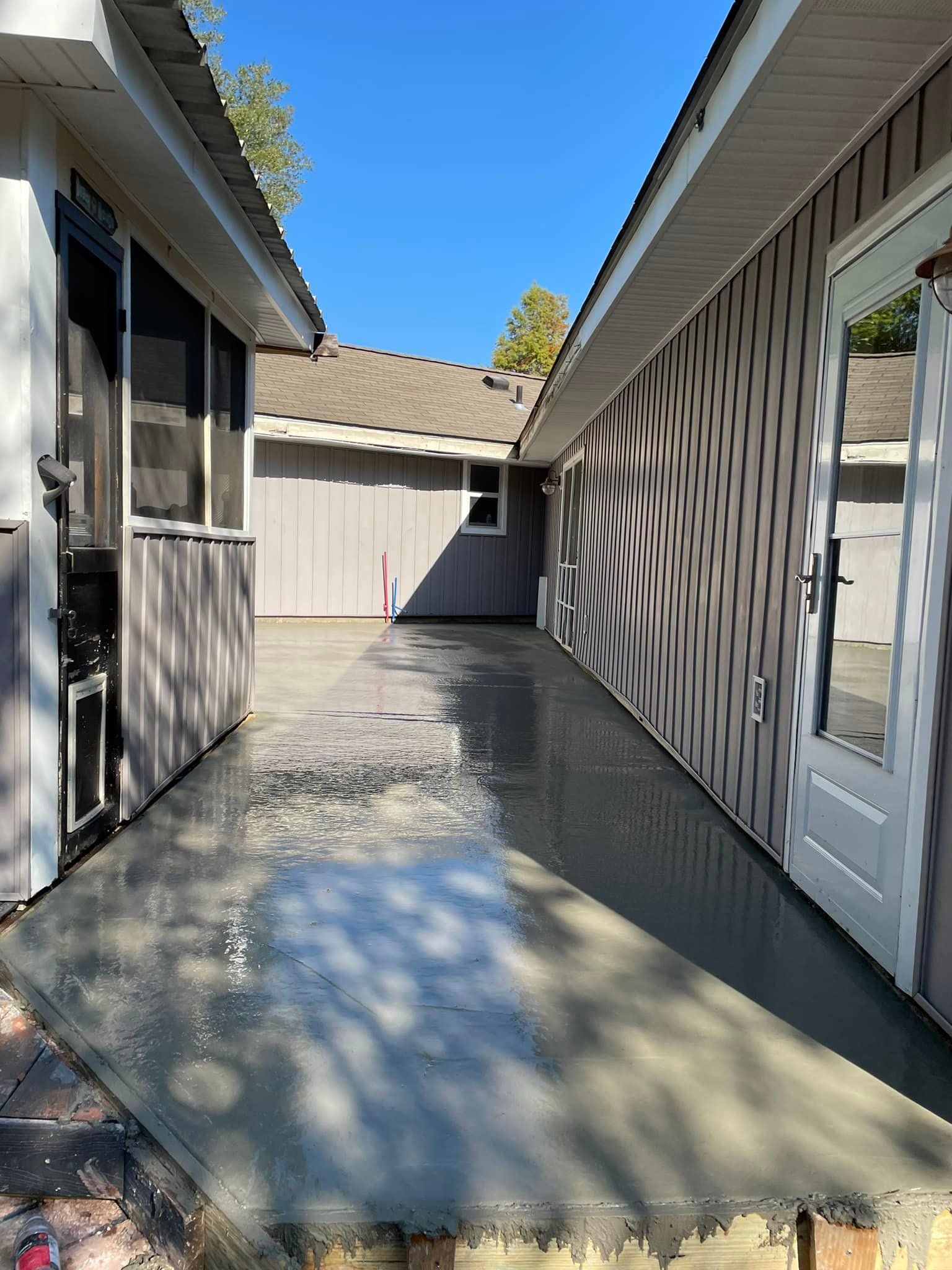 A freshly poured concrete patio walkway between two buildings under a clear blue sky.