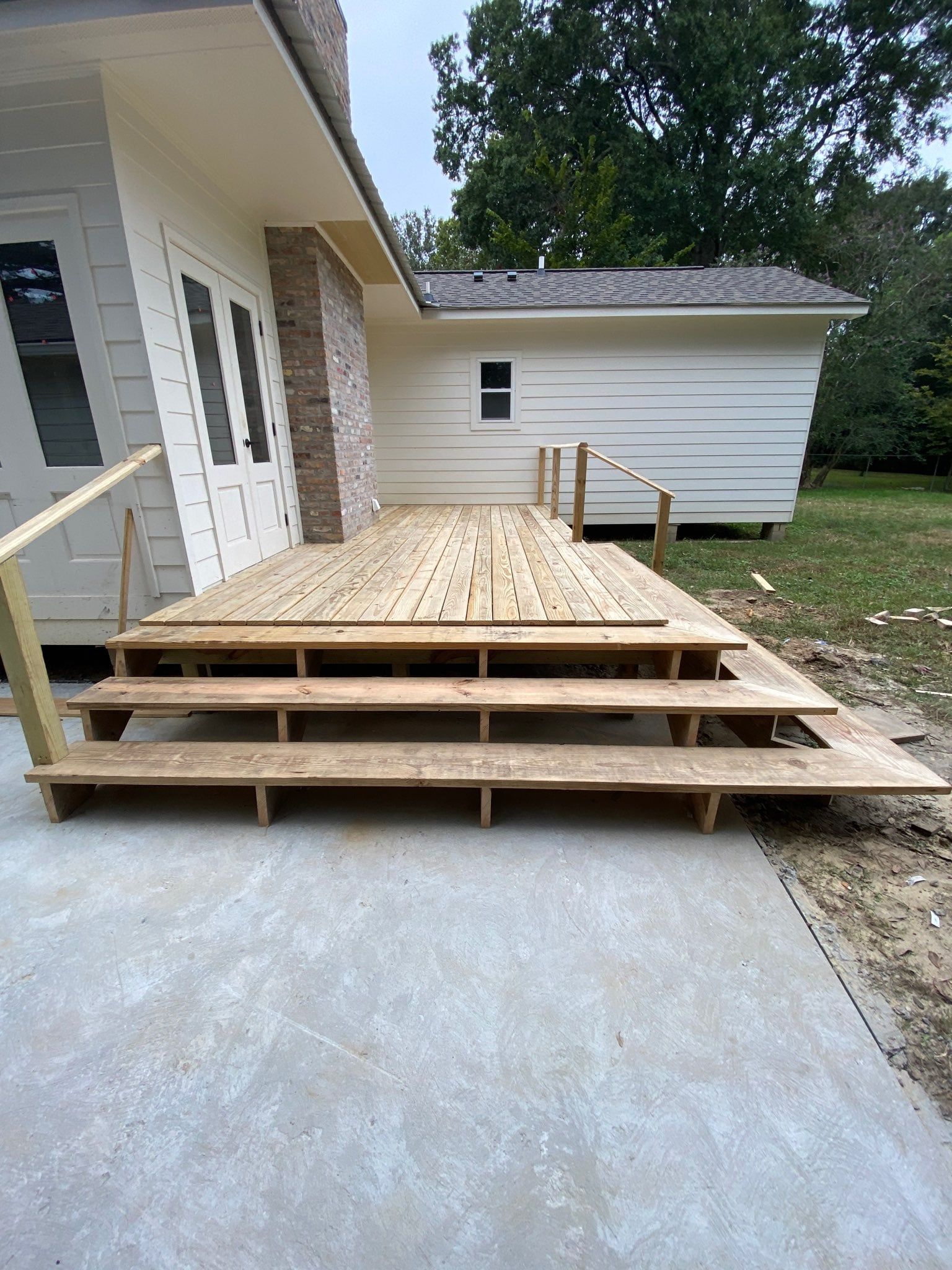 Newly constructed wooden deck with steps leading from a white house to a concrete patio.