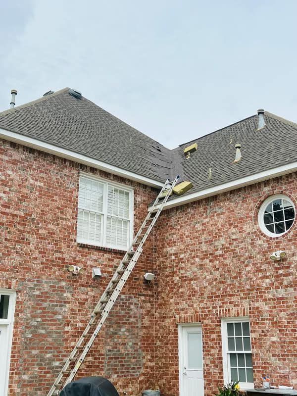 An extension ladder leans against a brick house, reaching a roof section where maintenance work is being performed.