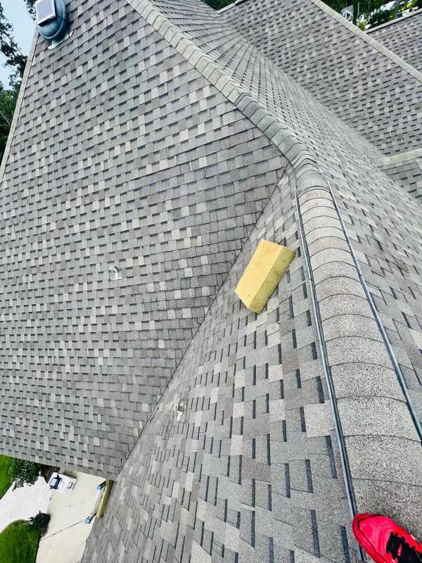 An aerial view of a gray asphalt shingle roof with a small yellow rectangular object sitting on one slope.