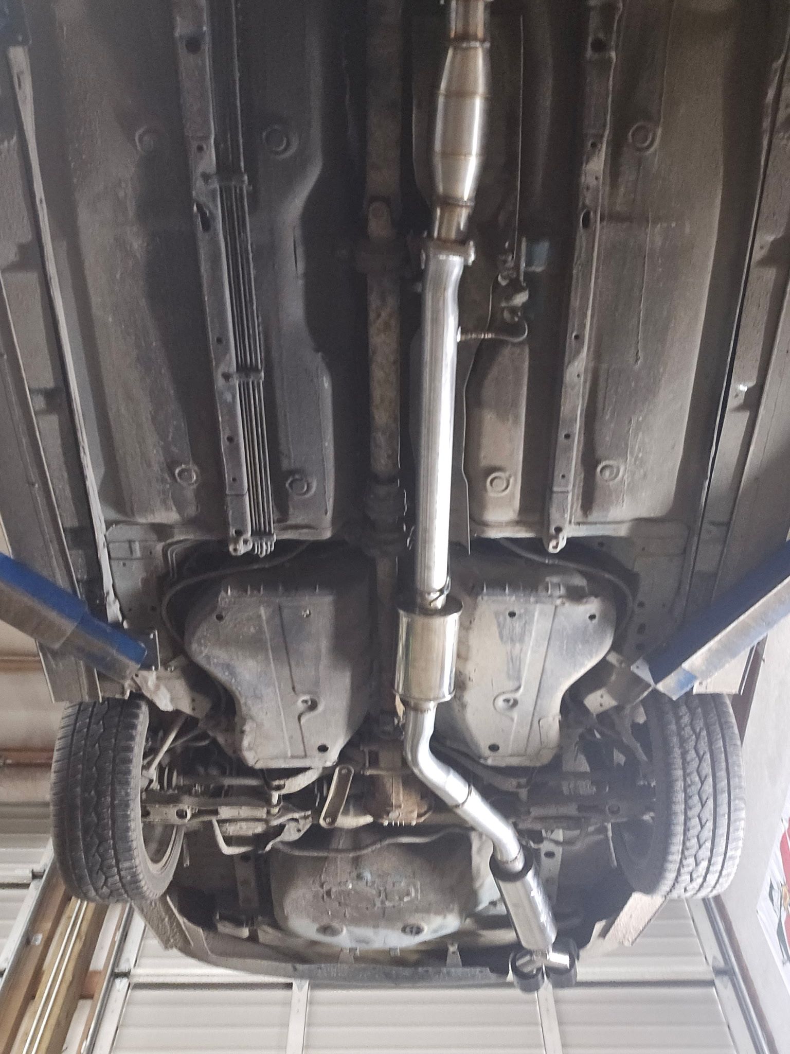Undercarriage of a car on a lift, showing exhaust system, rear axle, and wheels.