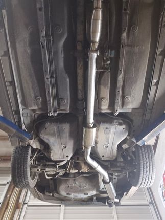 Undercarriage of a car on a lift, showing exhaust system, rear axle, and wheels.