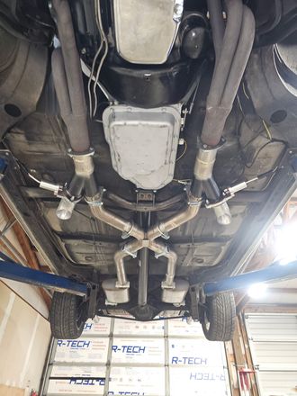 Undercarriage of a car on a lift, showing exhaust and drivetrain in a garage workshop