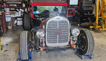Vintage red hot rod car parked in a garage, front view with exposed wheels and chrome grille