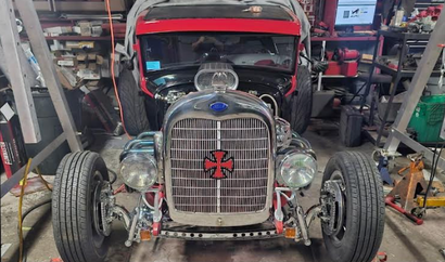 Custom vintage hot rod in a garage, front view with exposed engine and red hood open.